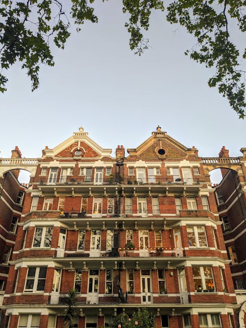 The image shows a row of historic red brick residential buildings situated along a quiet street, with multiple stories featuring large sash windows and decorative iron railings on the balconies. The b